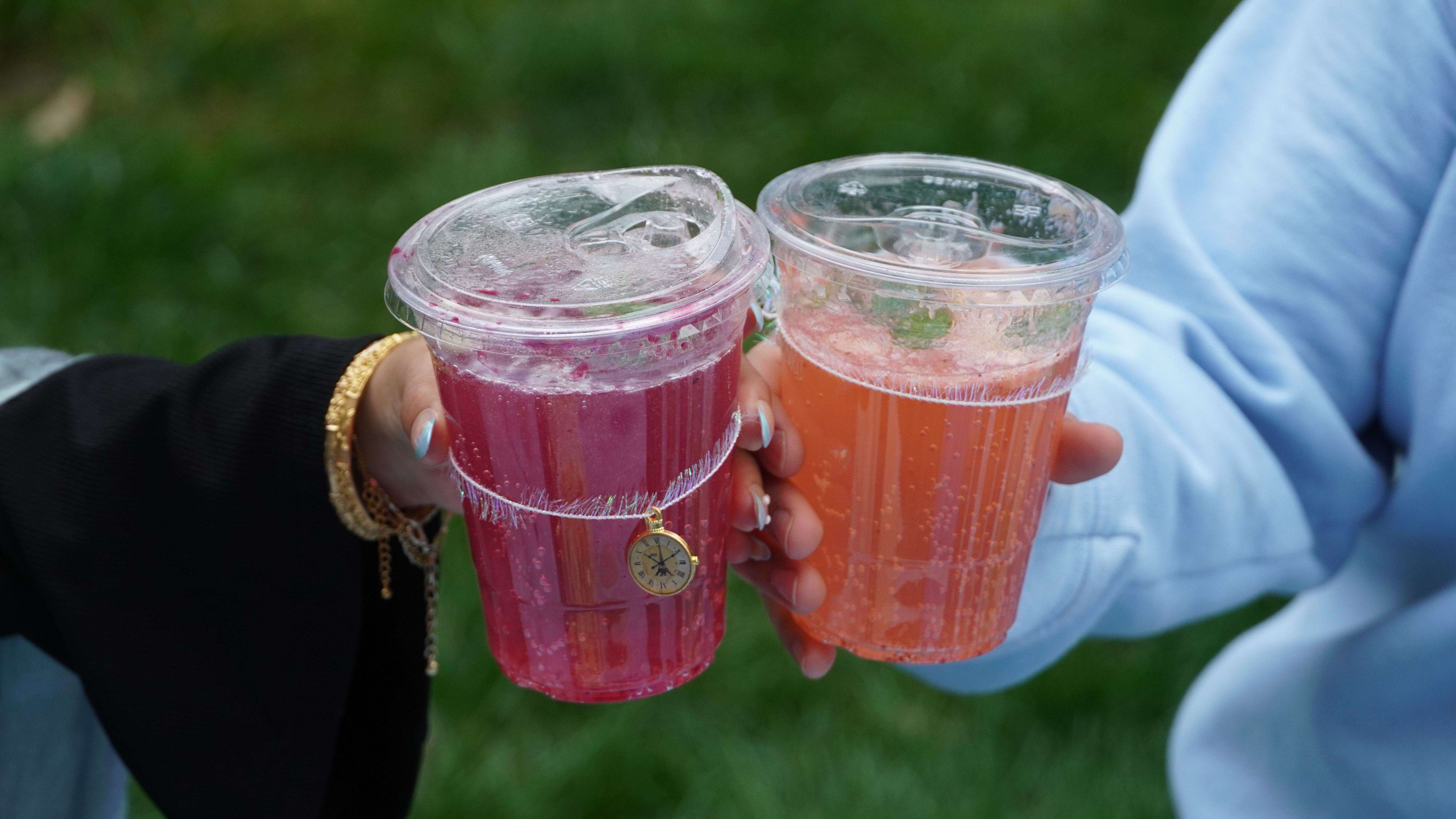 Close-up of hands holding vibrant drinks with gold accessories